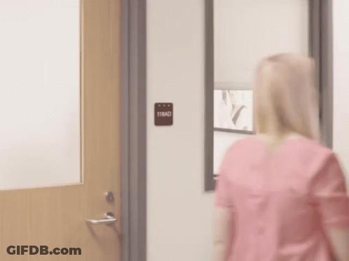 A Man In A Scrub Is Standing In A Doorway . GIF
