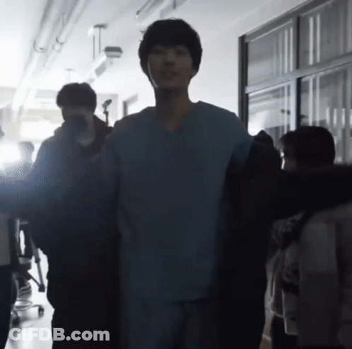 A Man In A Scrub Top Is Standing In A Hallway With A Group Of People GIF