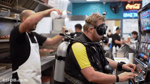 A Man In A Scuba Suit Is Playing A Slot Machine In A Restaurant GIF