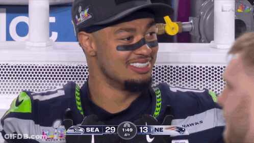 A Man In A Seahawks Jersey Is Smiling While Watching A Game GIF