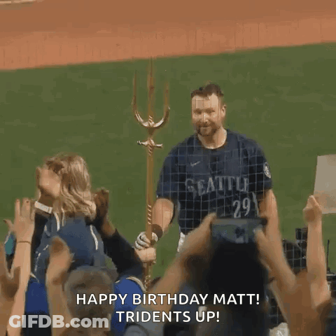 A Man In A Seattle Jersey Is Standing On A Baseball Field With A Trident In His Hand . GIF
