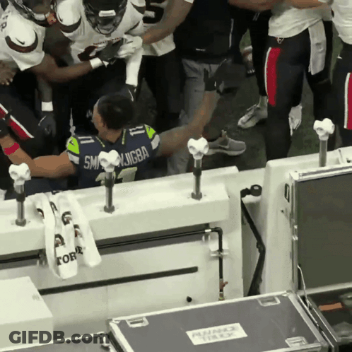 A Man In A Seattle Seahawks Jersey Is Surrounded By Other People GIF