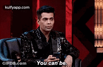 A Man In A Sequined Jacket Is Sitting In A Chair Holding A Cell Phone And Saying `` You Can Be . '' GIF