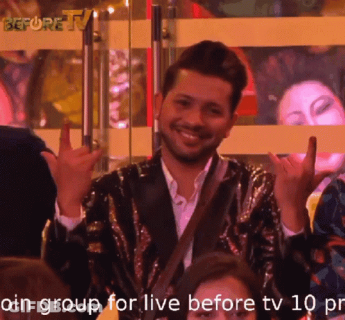 A Man In A Sequined Jacket Is Smiling And Making A Devil Horns Sign GIF
