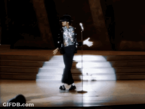 A Man In A Sequined Shirt Is Dancing On A Stage In Front Of A Microphone GIF