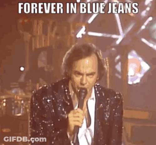 A Man In A Sequined Suit Is Singing Into A Microphone On Stage . GIF