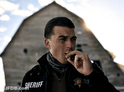 A Man In A Sheriff 'S Jacket Talks On A Walkie Talkie GIF