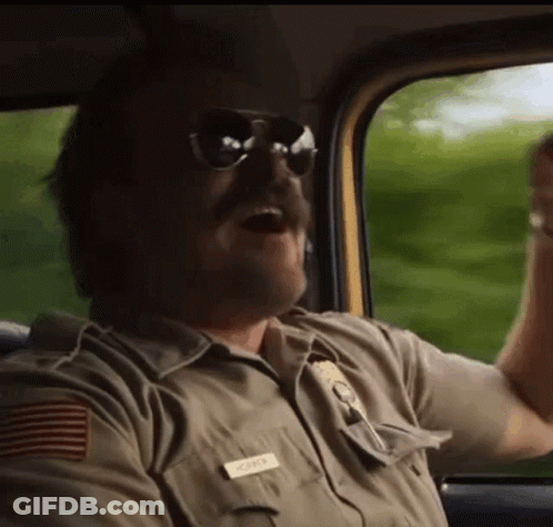 A Man In A Sheriff 'S Uniform And Sunglasses Is Driving A Car . GIF