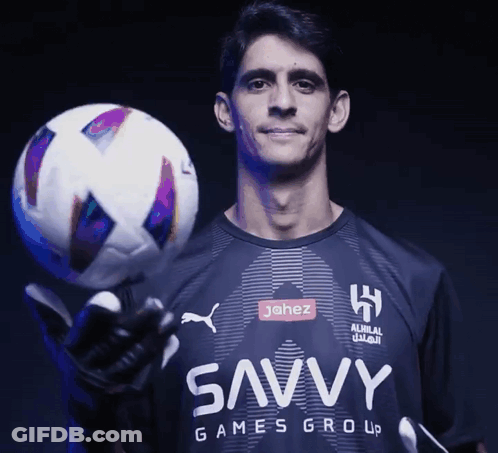 A Man In A Shirt That Says Savvy Games Group Holds A Soccer Ball GIF