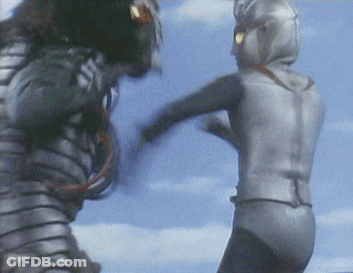 A Man In A Silver Suit Kicks Another Man In A Black Suit GIF