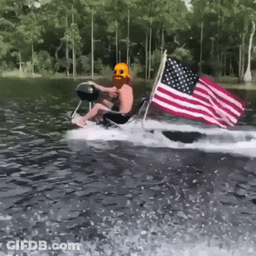 A Man In A Skull Mask Is Riding A Boat With An American Flag GIF