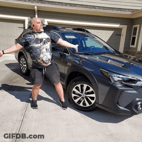 A Man In A Skull Shirt Stands In Front Of A Subaru GIF