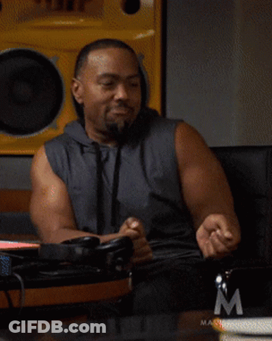 A Man In A Sleeveless Hoodie Is Sitting In Front Of A Masterclass Logo GIF