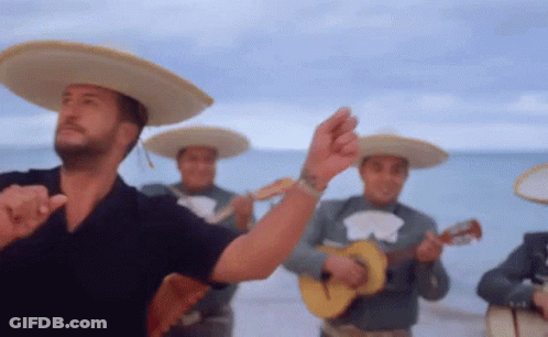 A Man In A Sombrero Is Dancing In Front Of A Band Of Mariachi Players GIF