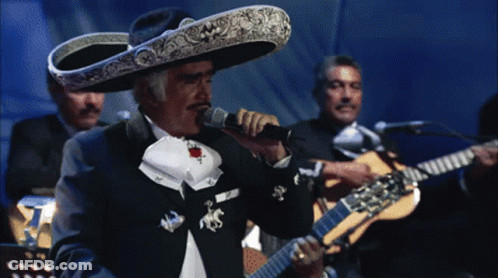 A Man In A Sombrero Sings Into A Microphone While Another Man Plays Guitar GIF