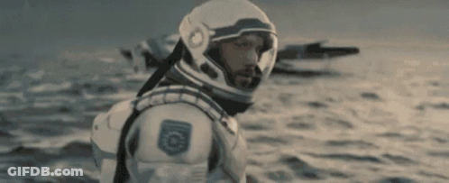 A Man In A Space Suit And Helmet Is Standing In The Ocean . GIF