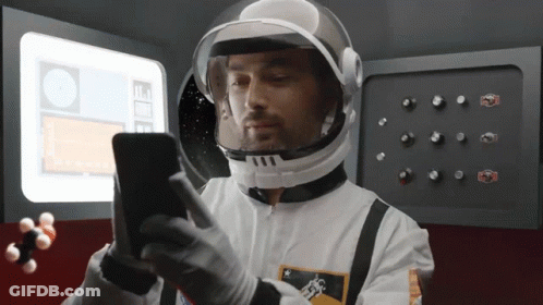 A Man In A Space Suit Is Looking At His Cell Phone GIF