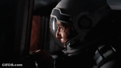A Man In A Space Suit Is Smoking A Cigarette In A Room . GIF