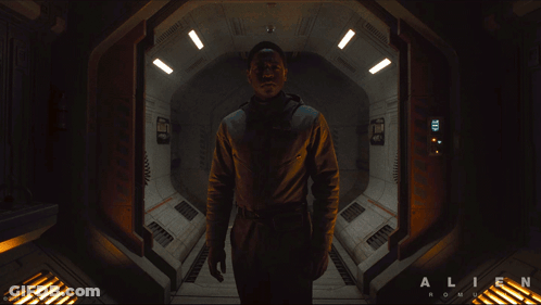 A Man In A Space Suit Is Standing In A Hallway That Says Alien On The Bottom GIF