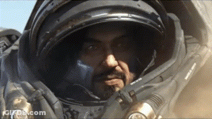 A Man In A Space Suit Looks At The Camera With His Hand On His Chin GIF
