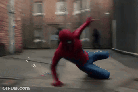 A Man In A Spiderman Costume Is Crawling On The Ground In Front Of A Brick Building . GIF