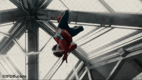 A Man In A Spiderman Costume Is Hanging Upside Down From A Metal Structure GIF