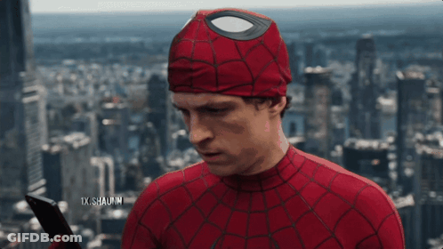 A Man In A Spiderman Costume Is Holding A Cell Phone In Front Of A City Skyline GIF