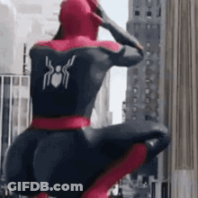 A Man In A Spiderman Costume Is Squatting Down In Front Of A Tall Building . GIF