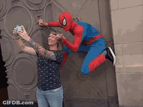 A Man In A Spiderman Costume Is Taking A Picture Of A Woman In A Tattooed Shirt . GIF