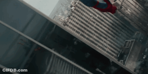 A Man In A Spiderman Suit Is Flying Through The Air Between Two Tall Buildings GIF
