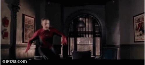 A Man In A Spiderman Suit Is Jumping In The Air In A Room . GIF