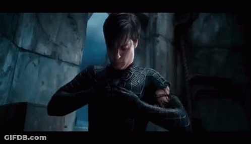 A Man In A Spiderman Suit Is Standing In A Dark Room With His Arms Outstretched . GIF
