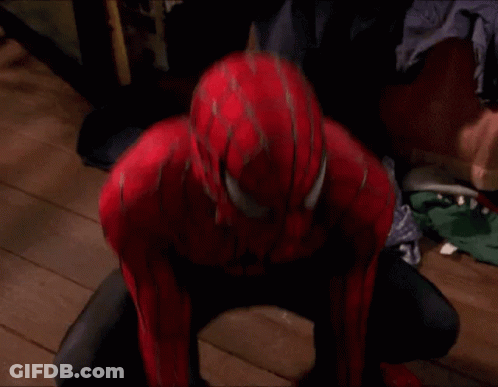 A Man In A Spiderman Suit Is Standing In A Room With A Brick Wall . GIF