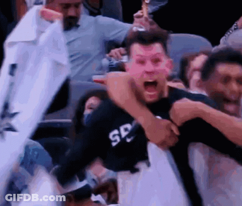 A Man In A Spurs Shirt Is Being Held By A Man In A Black Shirt . GIF