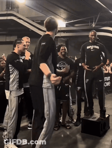 A Man In A Spurs Shirt Stands In Front Of A Crowd Of People GIF