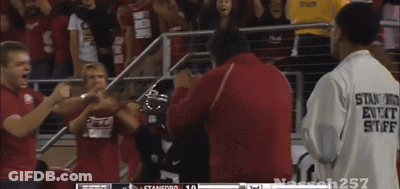 A Man In A Stanford Shirt Stands In Front Of A Crowd Of People GIF