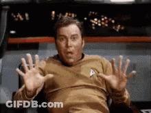 A Man In A Star Trek Uniform Is Sitting In A Chair With His Hands Up . GIF