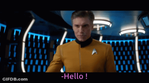 A Man In A Star Trek Uniform Says Hello In A Dark Room GIF