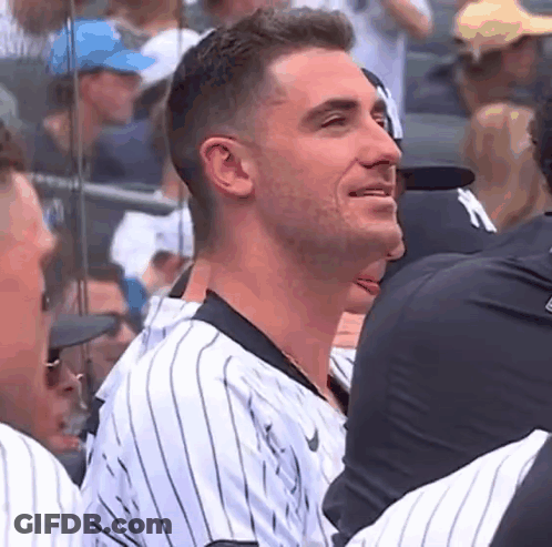 A Man In A Striped Baseball Uniform Is Sitting In A Stadium With Other People . GIF