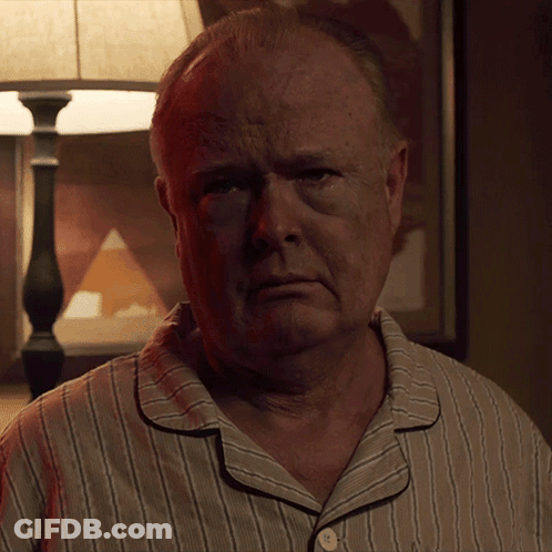 A Man In A Striped Pajama Shirt Looks At The Camera With A Lamp In The Background GIF