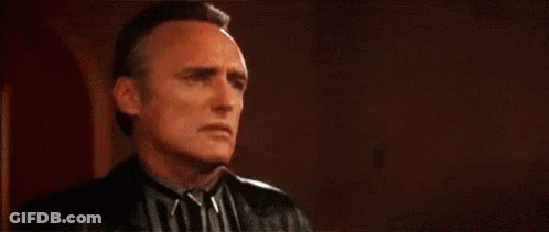 A Man In A Striped Shirt And Leather Jacket Is Looking At The Camera . GIF