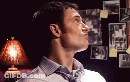 A Man In A Striped Shirt And Tie Is Looking Up In A Room With Pictures On The Wall . GIF