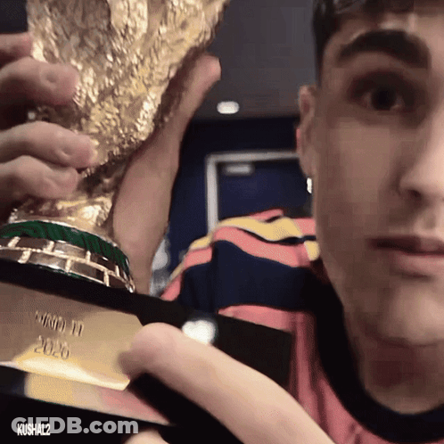 A Man In A Striped Shirt Holds A Trophy That Says World Cup 2020 GIF