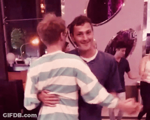 A Man In A Striped Shirt Hugs Another Man In A Blue Shirt GIF