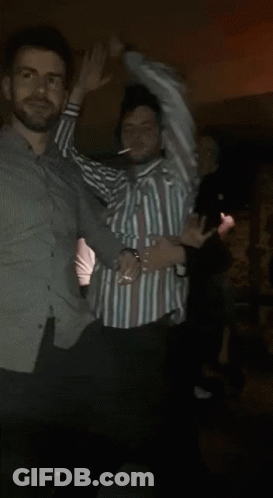 A Man In A Striped Shirt Is Dancing In A Crowd Of People GIF