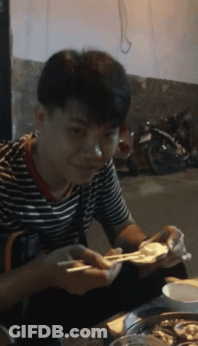 A Man In A Striped Shirt Is Eating Food With Chopsticks And Smiling GIF