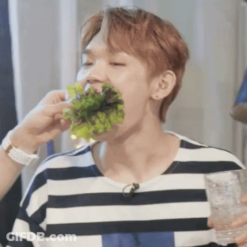 A Man In A Striped Shirt Is Eating Lettuce While Holding A Glass . GIF