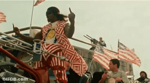A Man In A Striped Shirt Is Giving The Middle Finger While Riding A Motorcycle . GIF