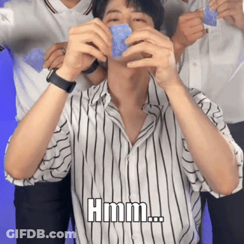 A Man In A Striped Shirt Is Holding A Blue Object In His Hands And Says Hmm GIF