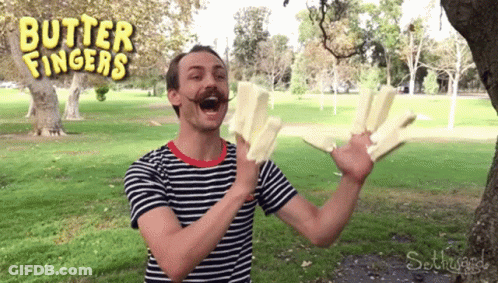 A Man In A Striped Shirt Is Holding A Piece Of Butter In Front Of A Sign That Says Butter Fingers GIF